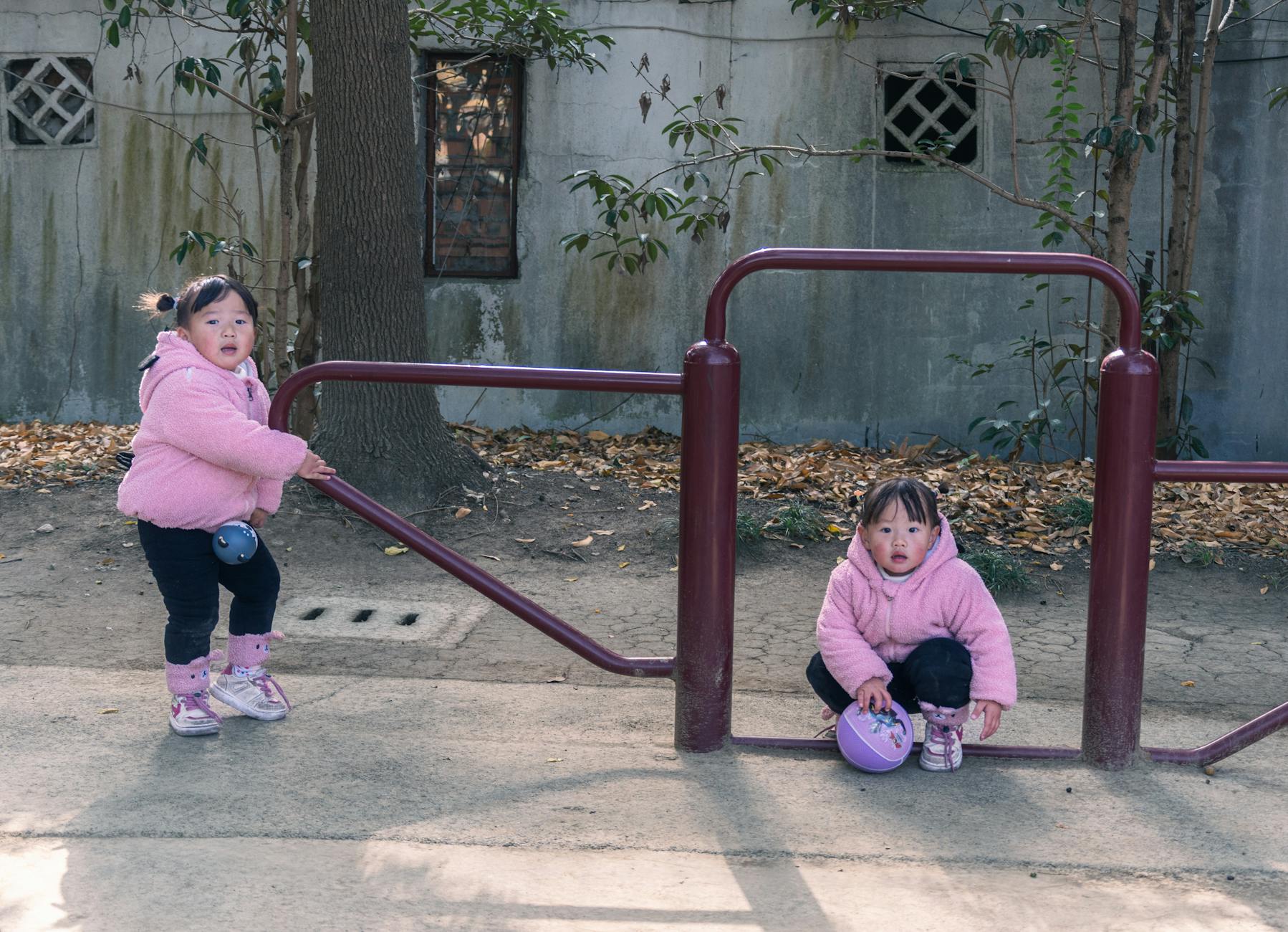 Dwoje dzieci w różowych kurtkach bawi się przy drabinkach w parku jesienią