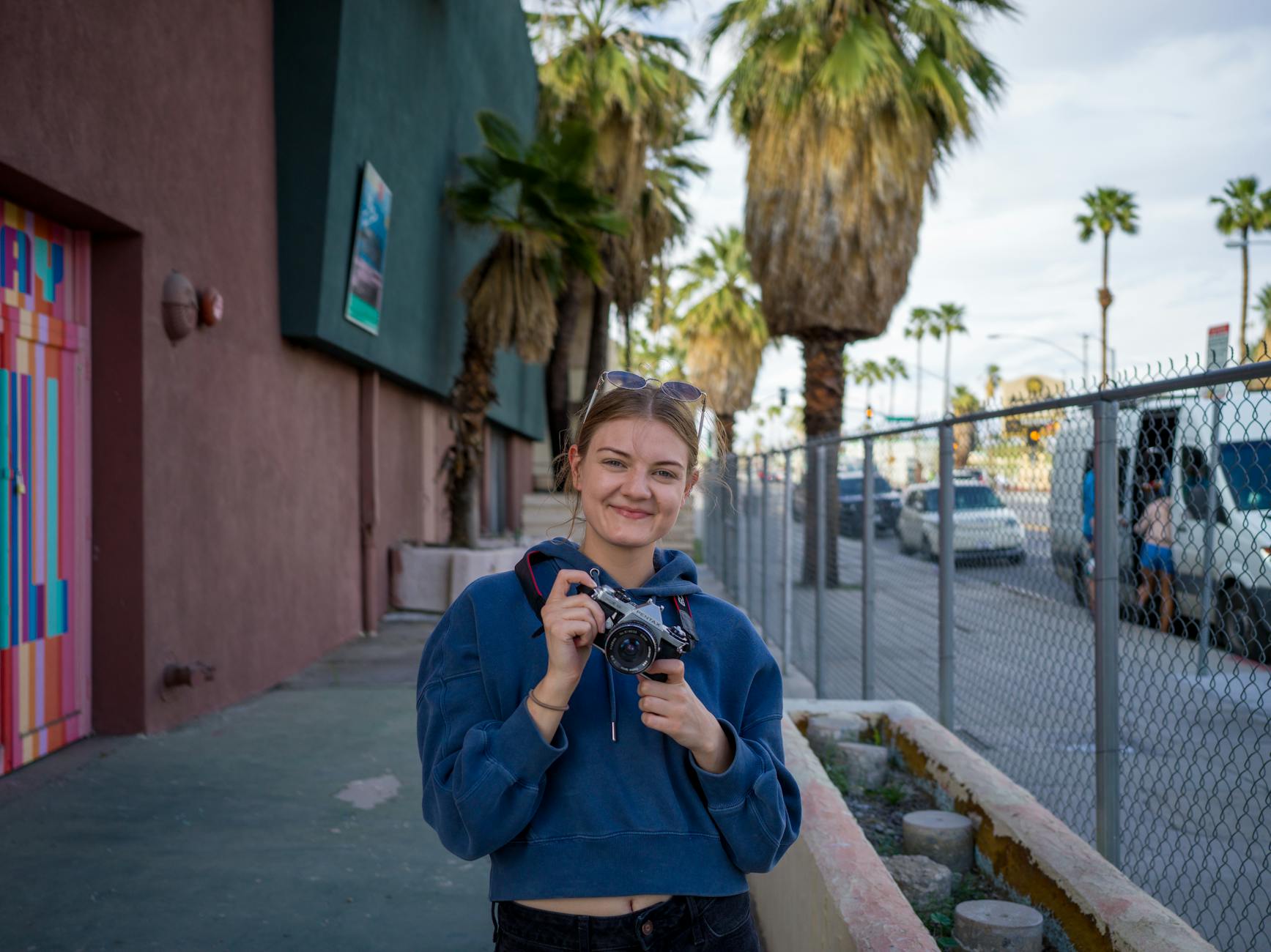 Uśmiechnięta młoda kobieta z analogowym aparatem na miejskiej ulicy