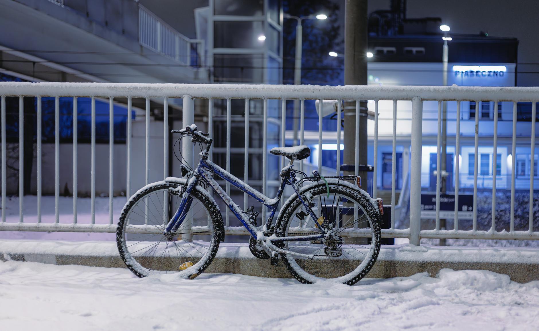Zaśnieżony rower przypięty do barierki nocą w centrum miasta
