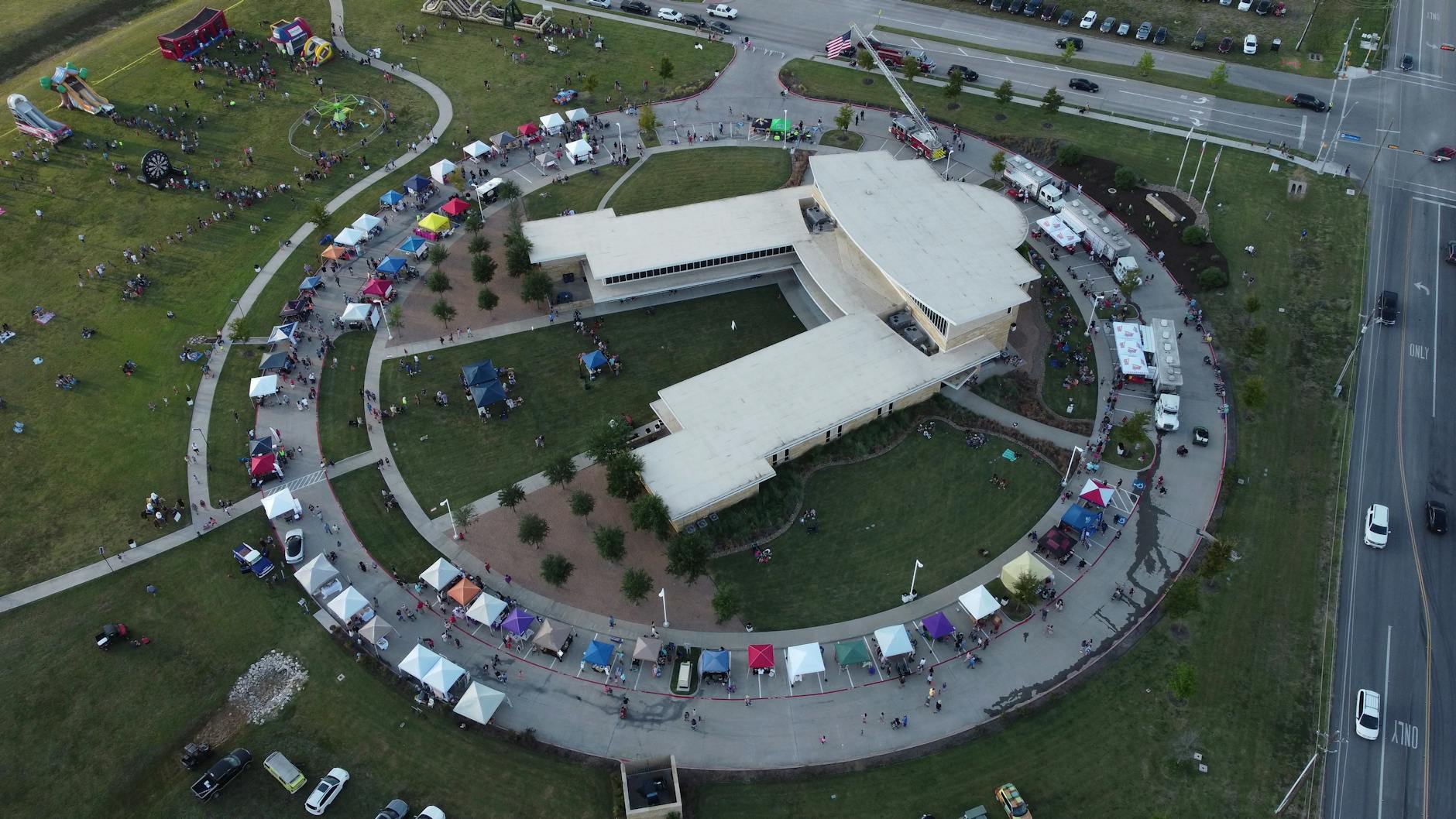 Widok z lotu ptaka na okrągły budynek otoczony festiwalowymi namiotami