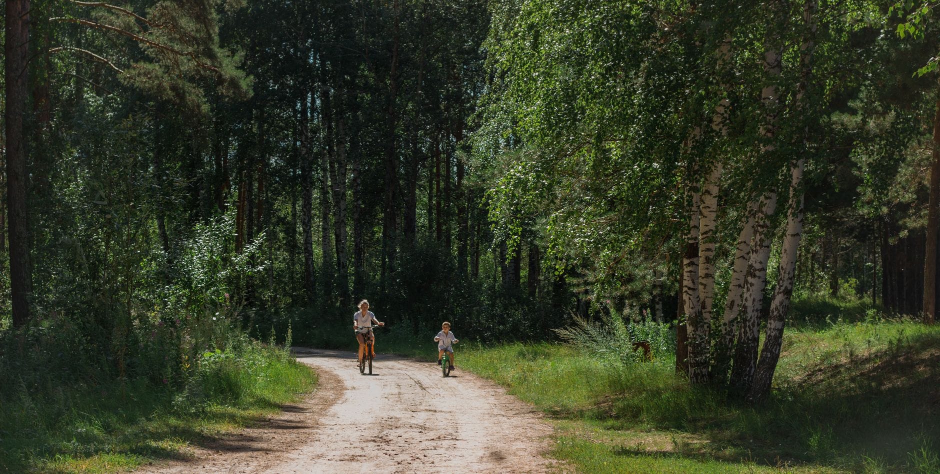 Mama z dzieckiem jadą na rowerze leśną ścieżką w słoneczny dzień