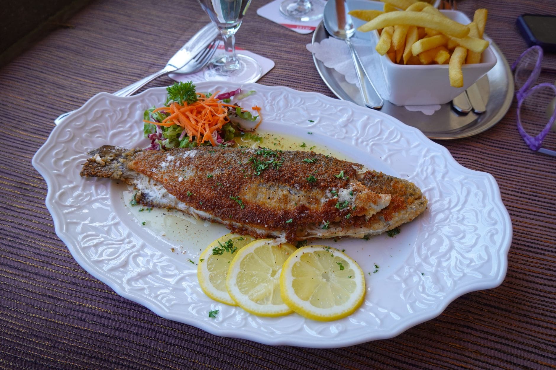 Grillowana ryba z cytryną, frytkami i sałatką na talerzu